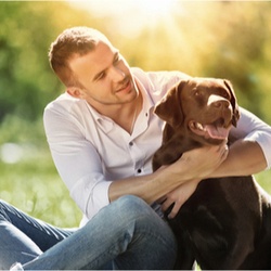 Young man sitting on the grass with a Retriever.